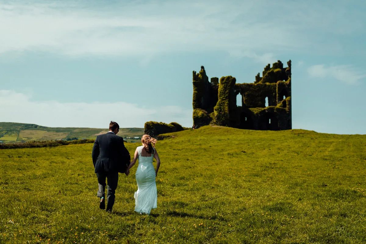 Couple walking through the meadows to a castle ruin for the ceremony of their destination wedding in Ireland