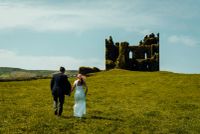 Couple walking through the meadows to a castle ruin for the ceremony of their destination wedding in Ireland