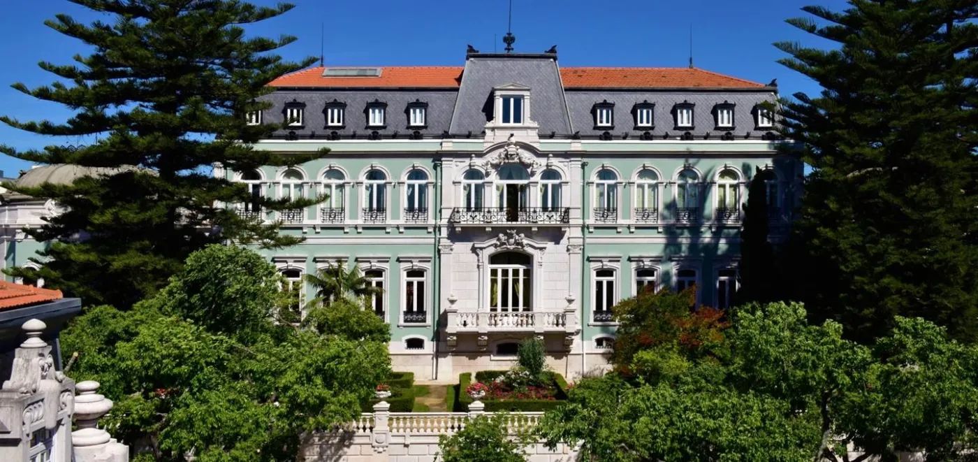 Facade of a gray, blue, and green palace with trees outside