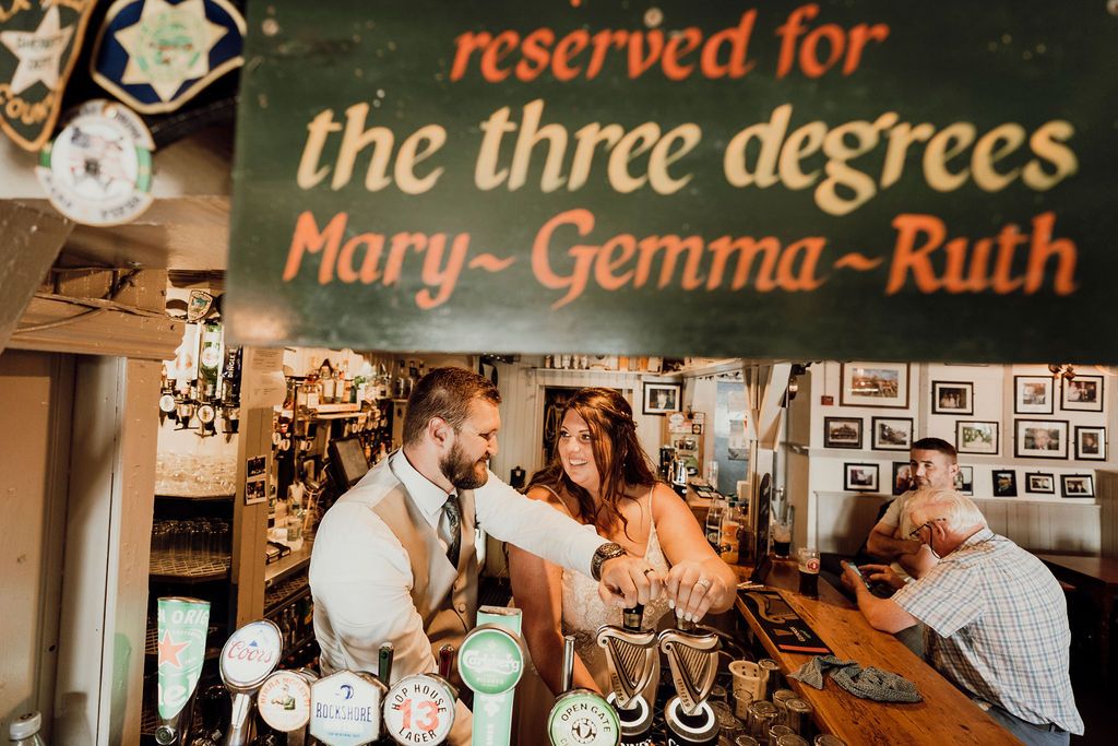 Bride and groom holding harp-shaped beer dispensers inside a traditional Irish pub to celebrate their elopement in Ireland