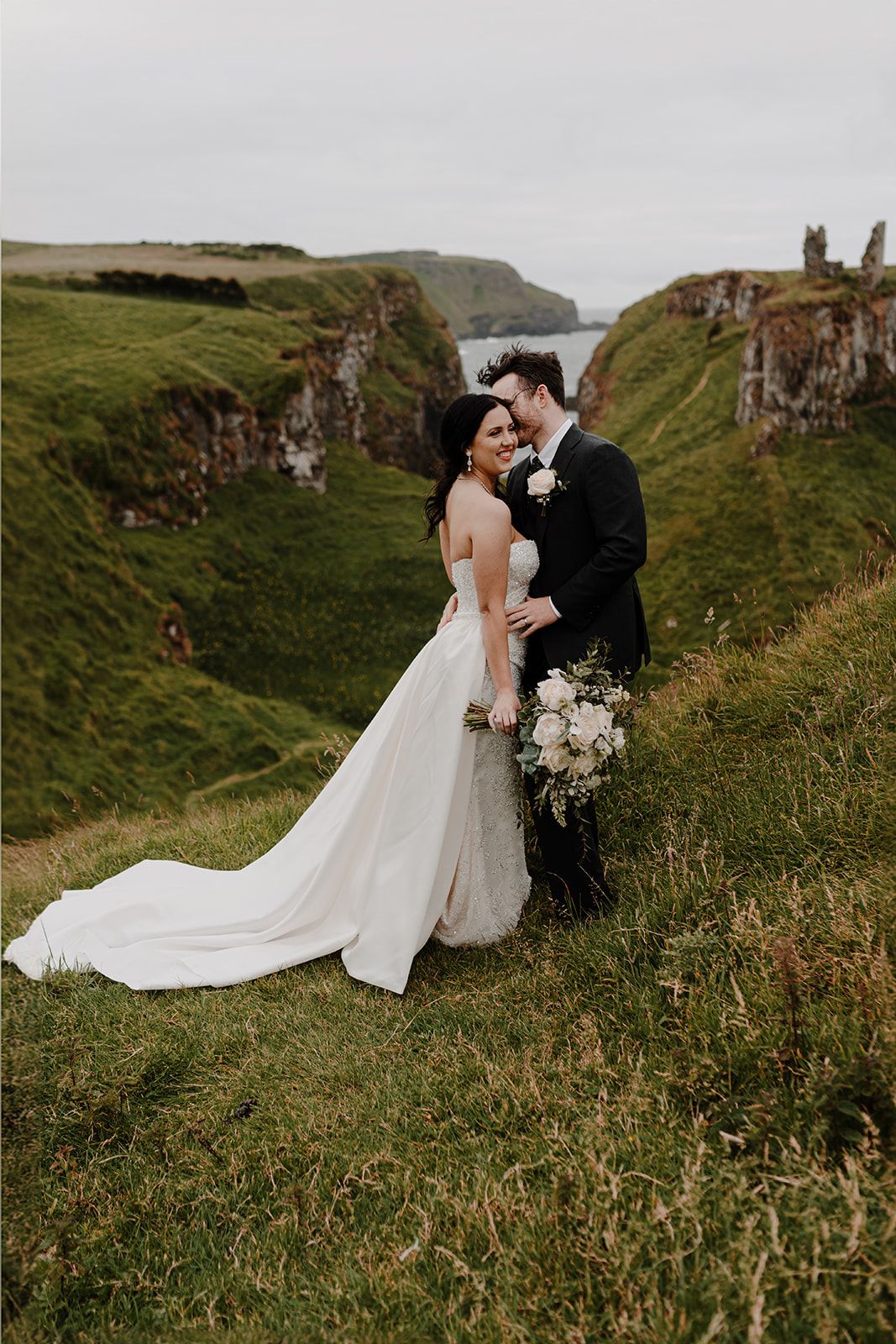 Bride and groom on top of a cliff with a castle ruin in the background during their elopement in Northern Ireland