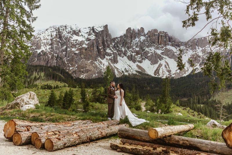 Bride and groom posing on wood logs with the Dolomite mountains in the background