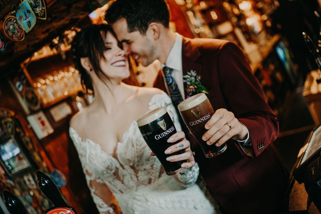 Newlyweds inside an Irish pub holding one glass each of Guinness beer as they celebrate their elopement in Ireland