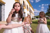 Little girls wearing white dresses blow bubbles outside the farmhouse during Megan and Zac's destination wedding in Spain
