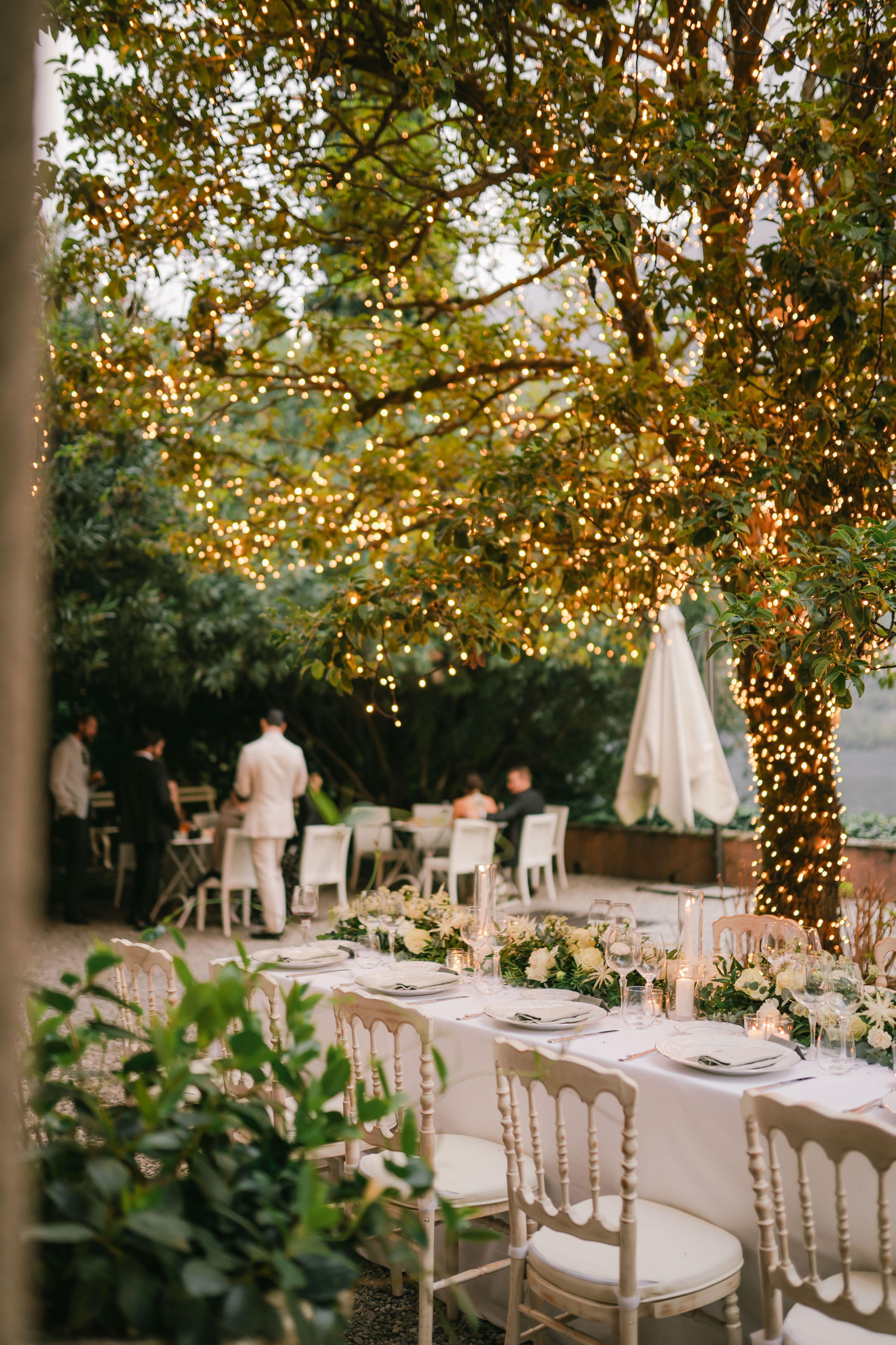 Lush green trees decorated with fairy lights with a long table and chairs for a Lake Como vow renewal reception in Italy