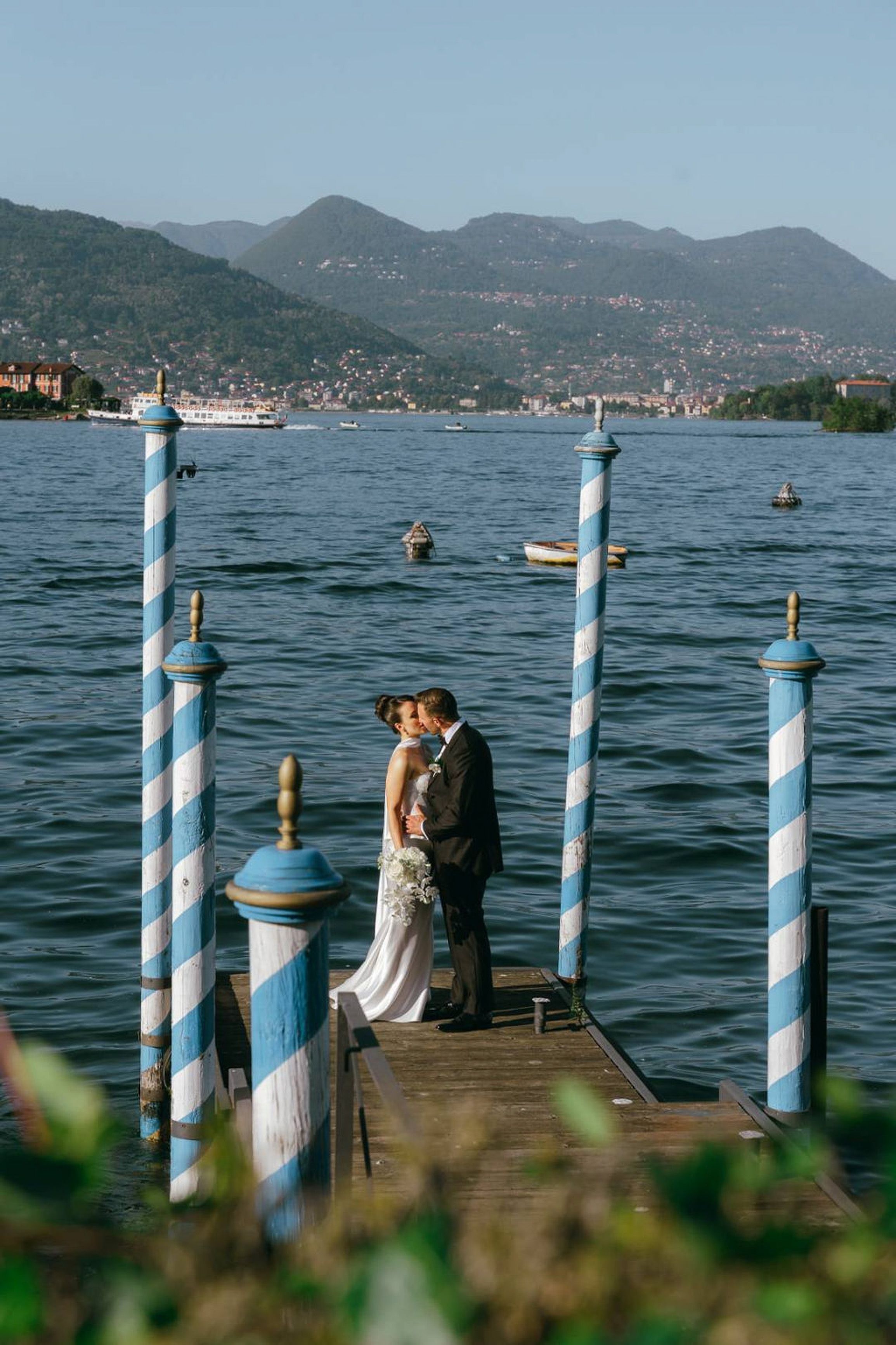 Newlyweds sharing a kiss on a lakeside pier at a small wedding in Italy with mountain views