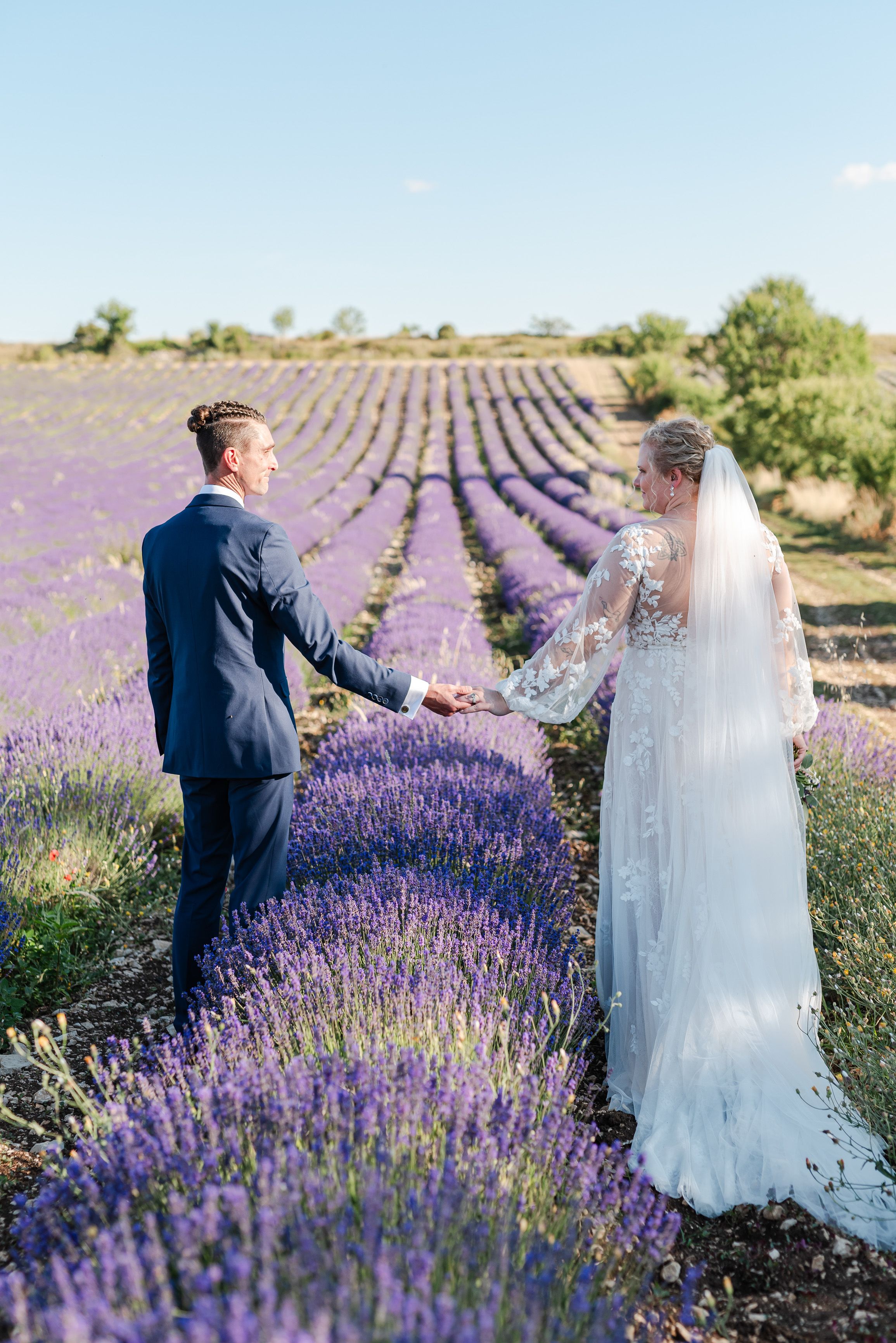 Newlyweds holding hands among blooming lavender rows at an intimate wedding in France
