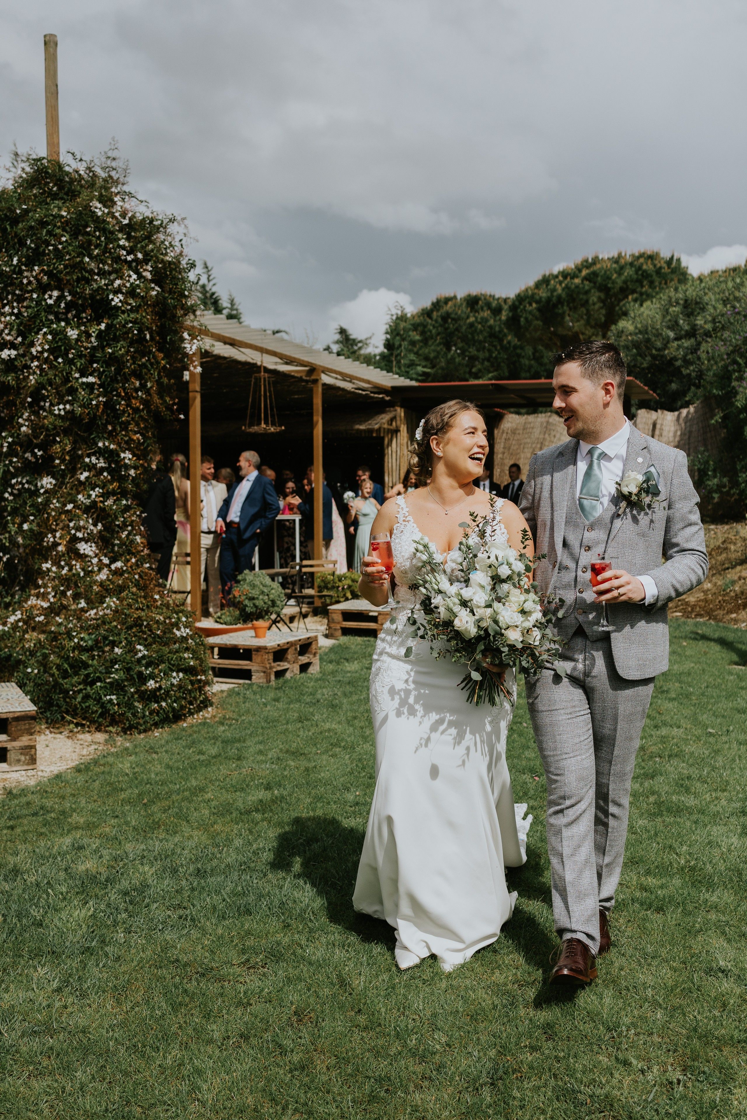 Bride and groom walking on a grassy area with their guests at the back during their destination wedding in Portugal