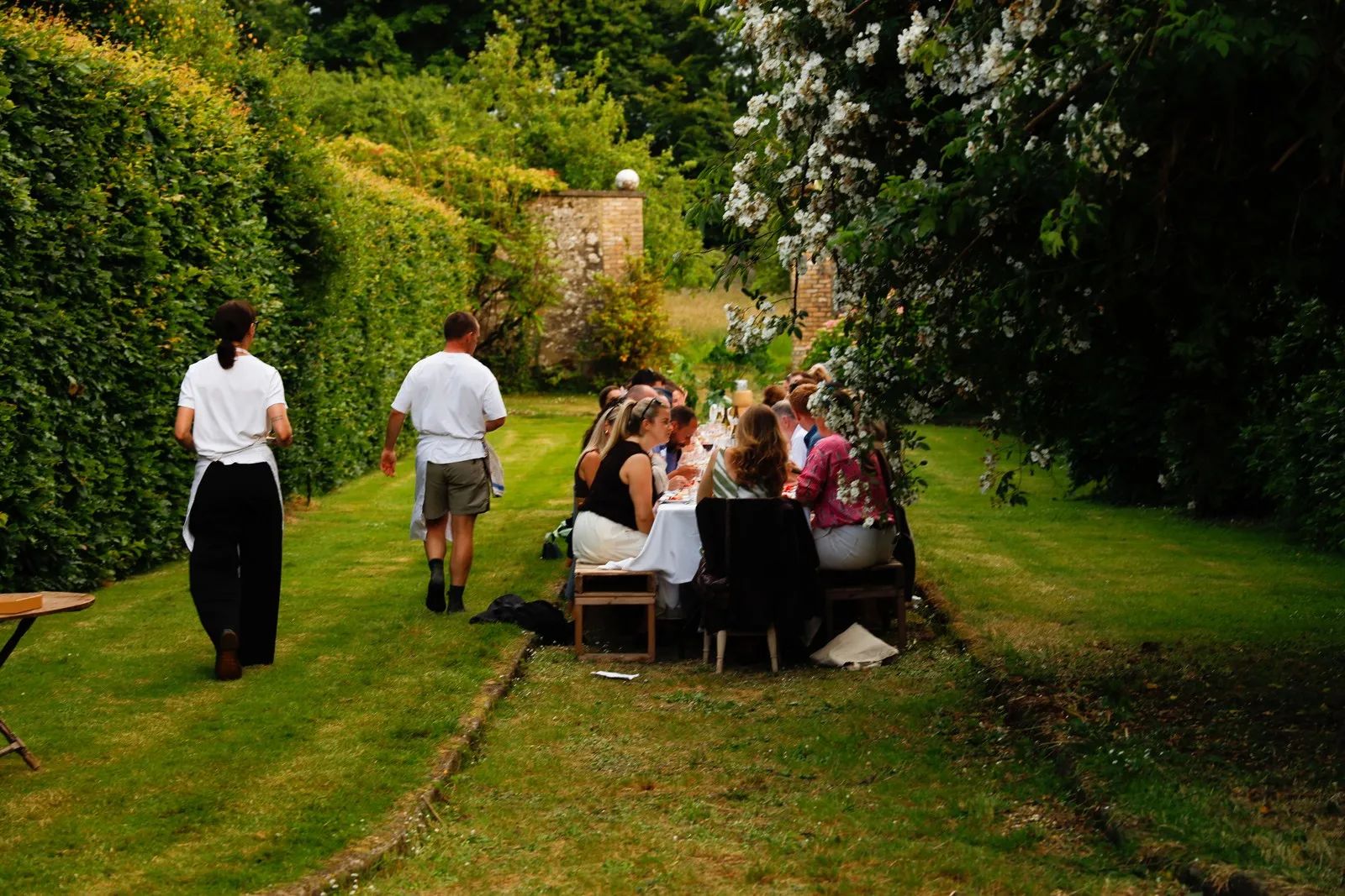 Guests are seated in a long table at a yard surrounded by lush greens in a castle for small weddings in Ireland