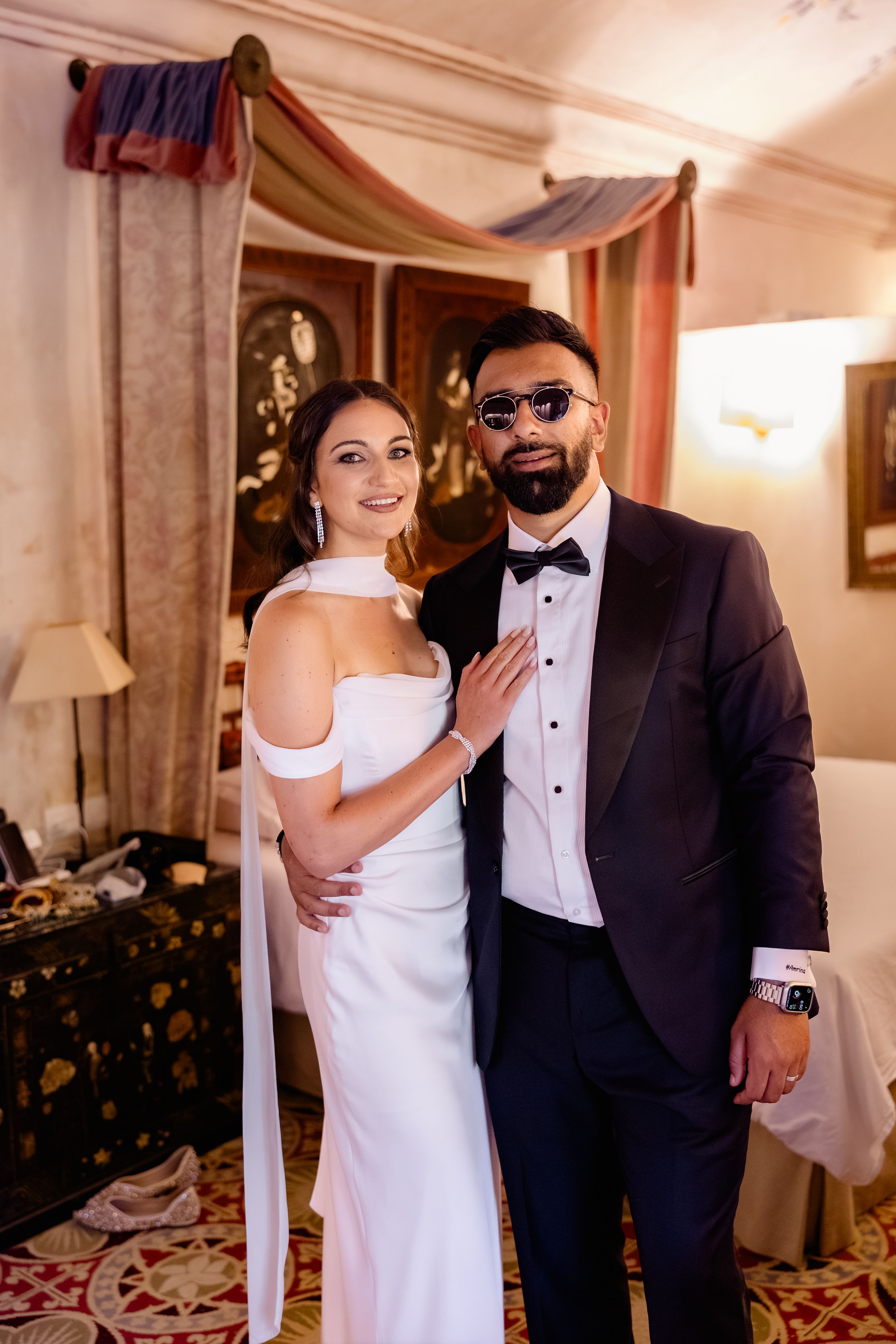 Bride and groom in semi-casual reception outfits inside a room looking at the camera