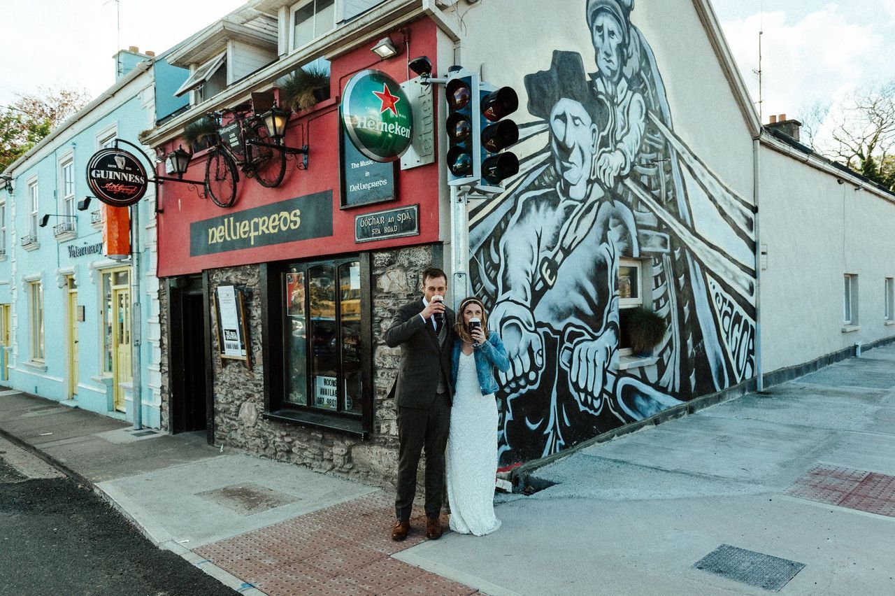 Newlyweds drinking a glass of Guinness beer outside on a bright afternoon during the photoshoot of their elopement in Ireland