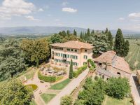 A country house in Florence with the lush green Tuscan countryside consisting of vineyards, trees, and medieval buildings