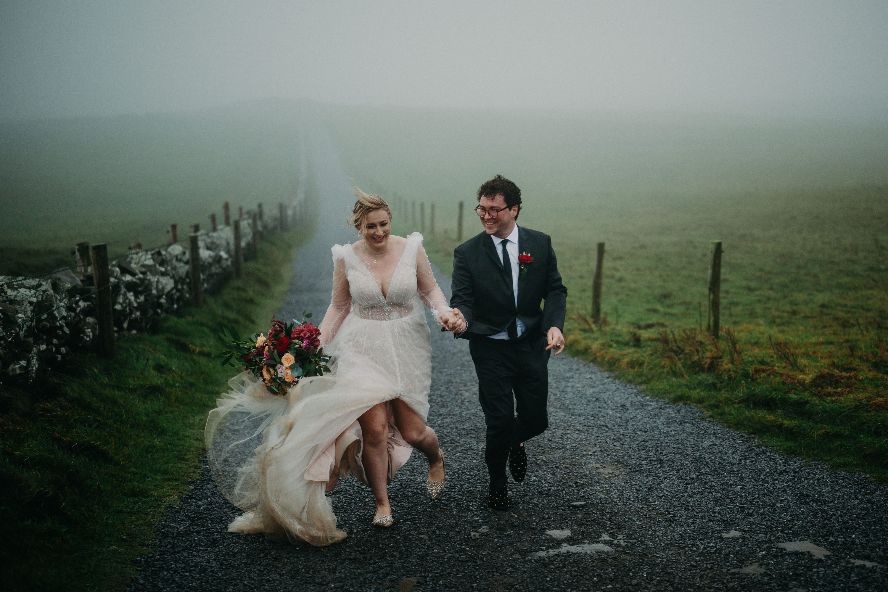 Joyful newlyweds running along a misty country road after a small wedding in Ireland celebration