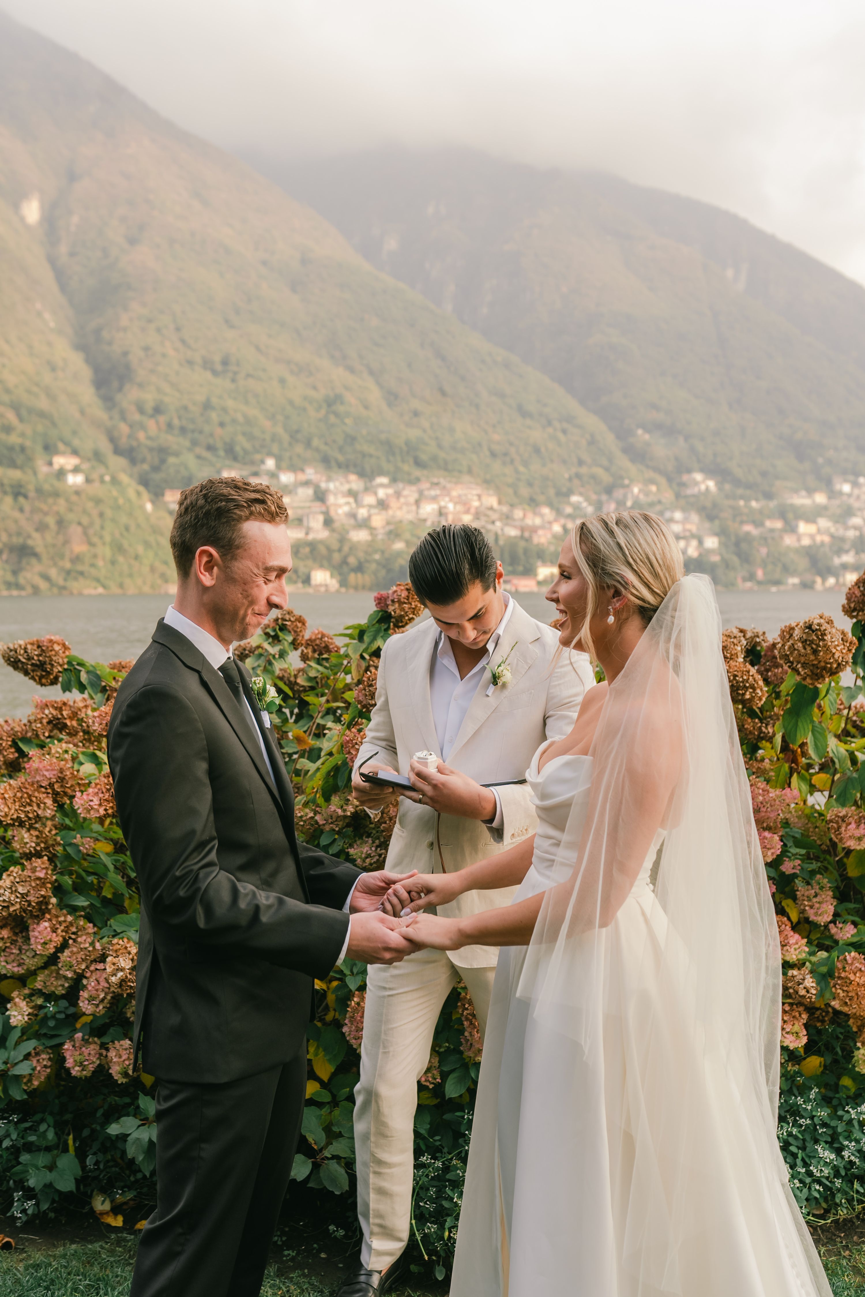 Bride and groom holding each other during a wedding ceremony in Italy with Lake Como and rolling hills in the background