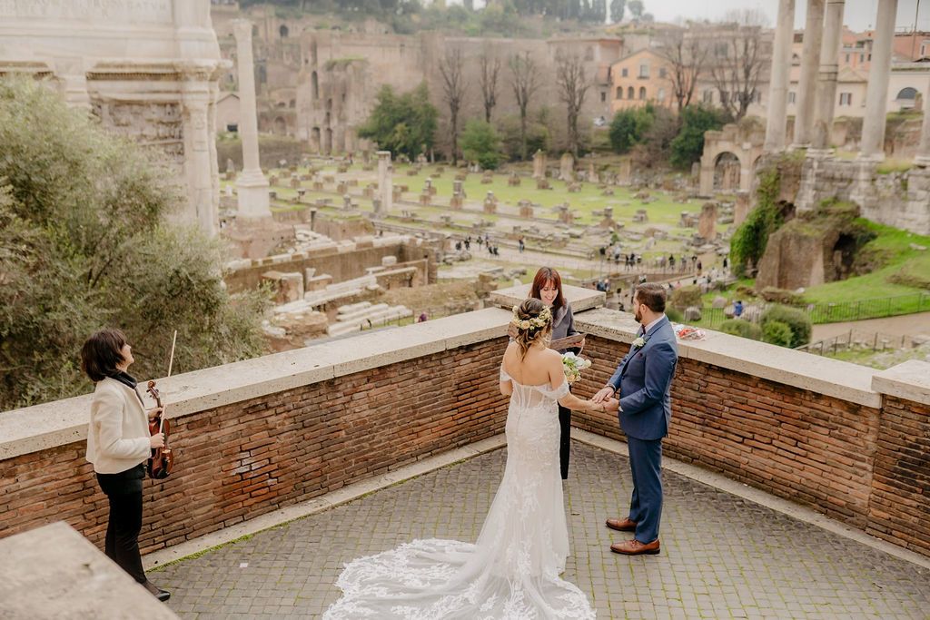 Bride and groom having an Italian elopement ceremony with their celebrant and a violinist on top of a terrace overlooking the Pantheon in Rome