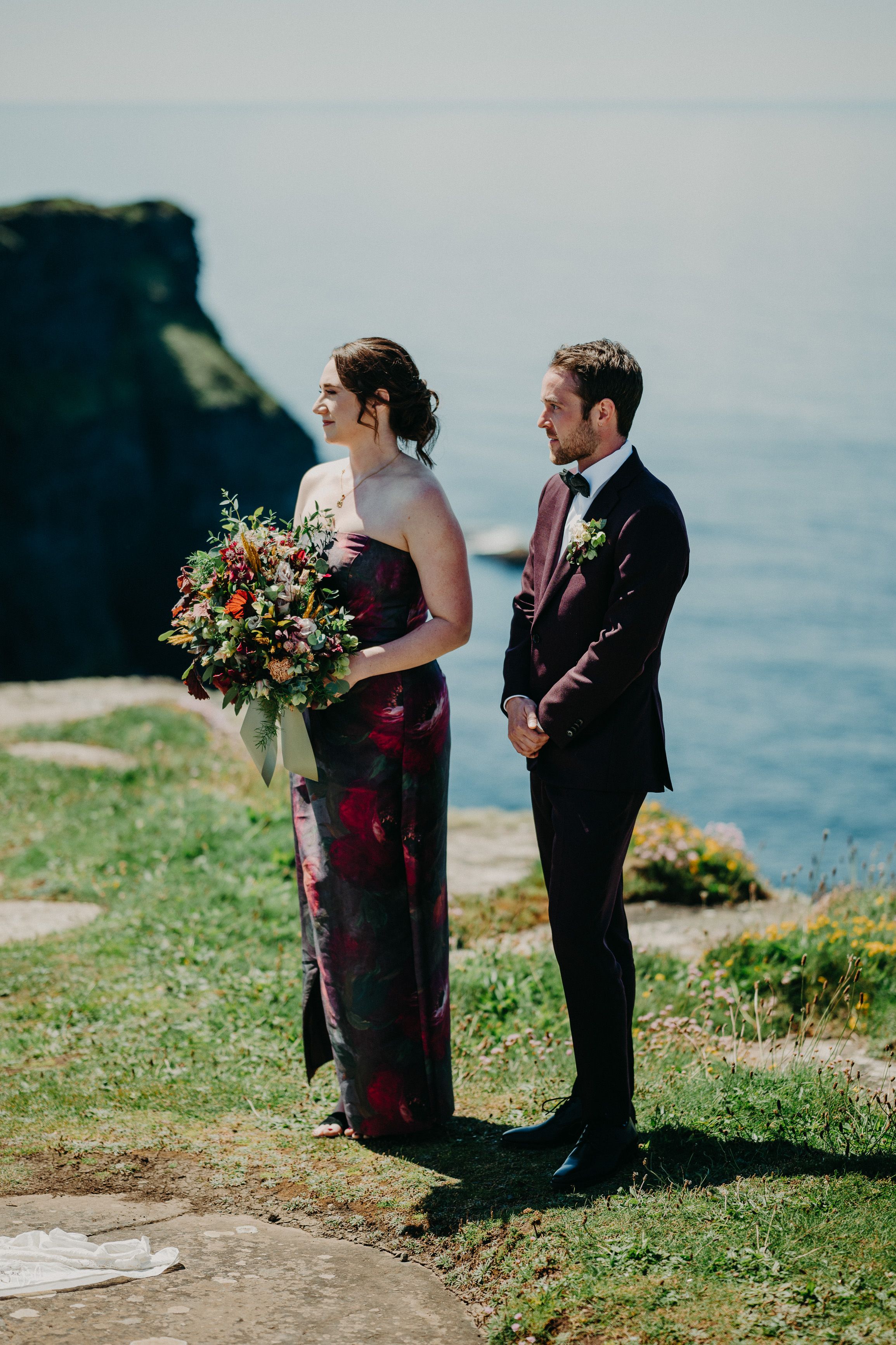 A groomsman and bridesmaid looking on the couple on top of a cliff during a small wedding in Ireland