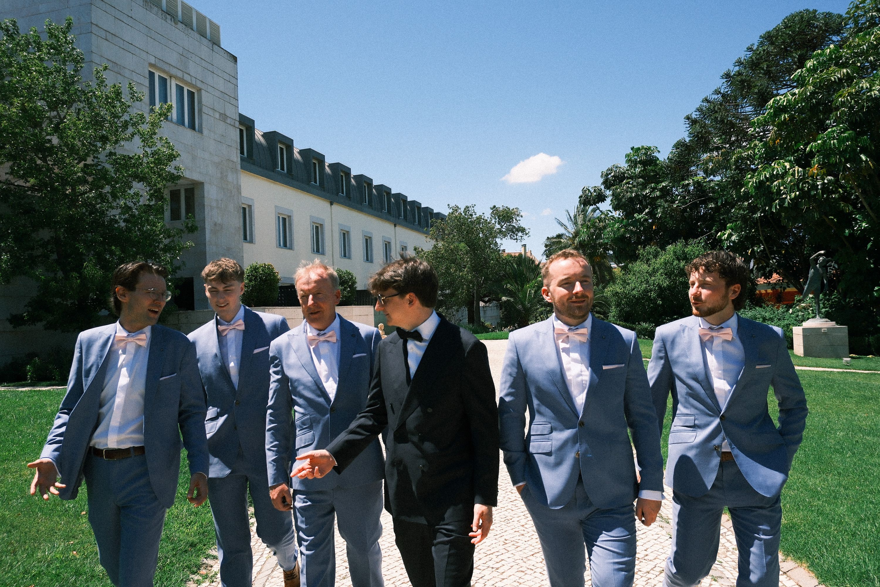 Groom walks with his groomsmen before a small wedding in Portugal at a sunlit garden venue