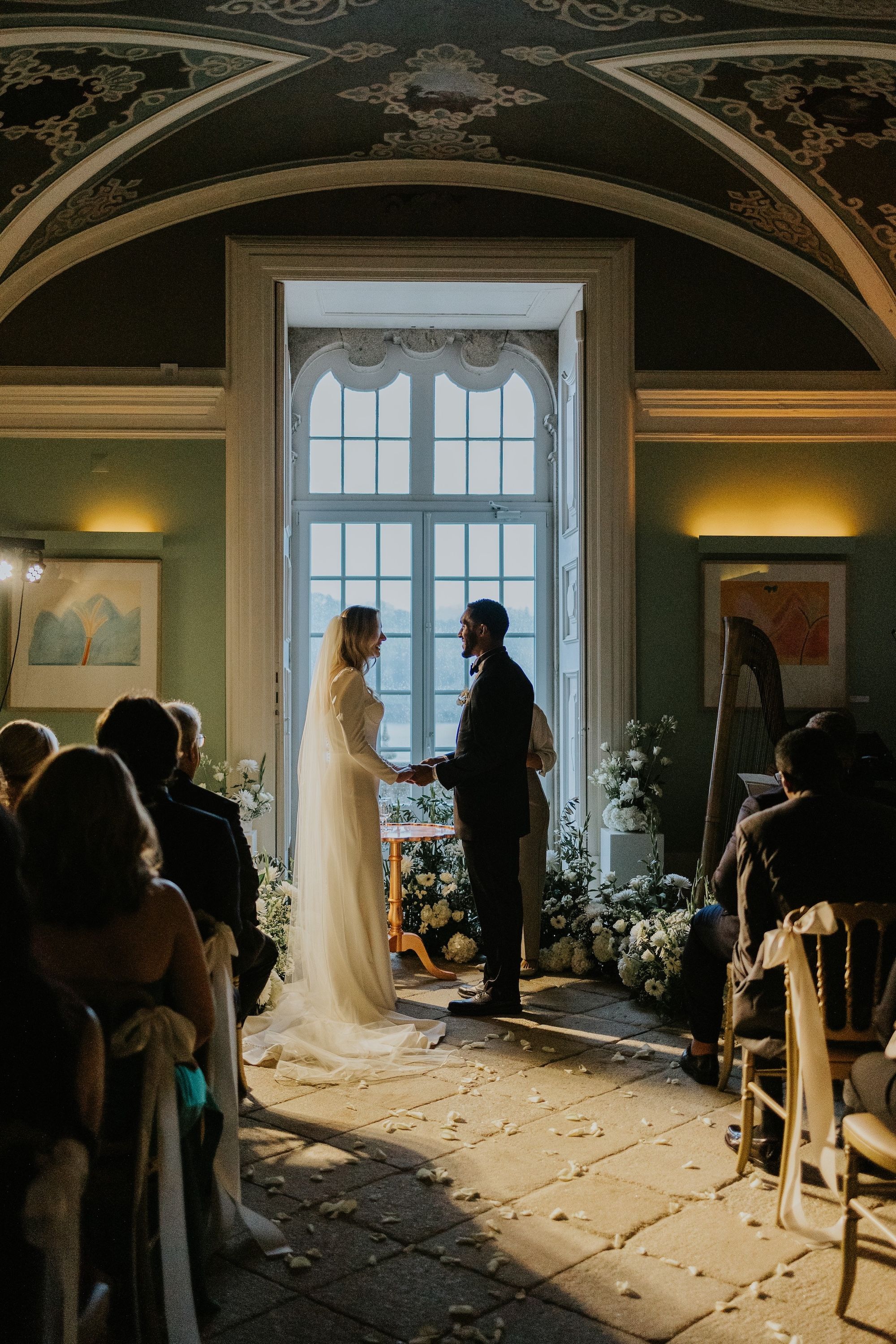 Bride and groom hold hands and face each other during the indoor ceremony of their intimate wedding in Portugal