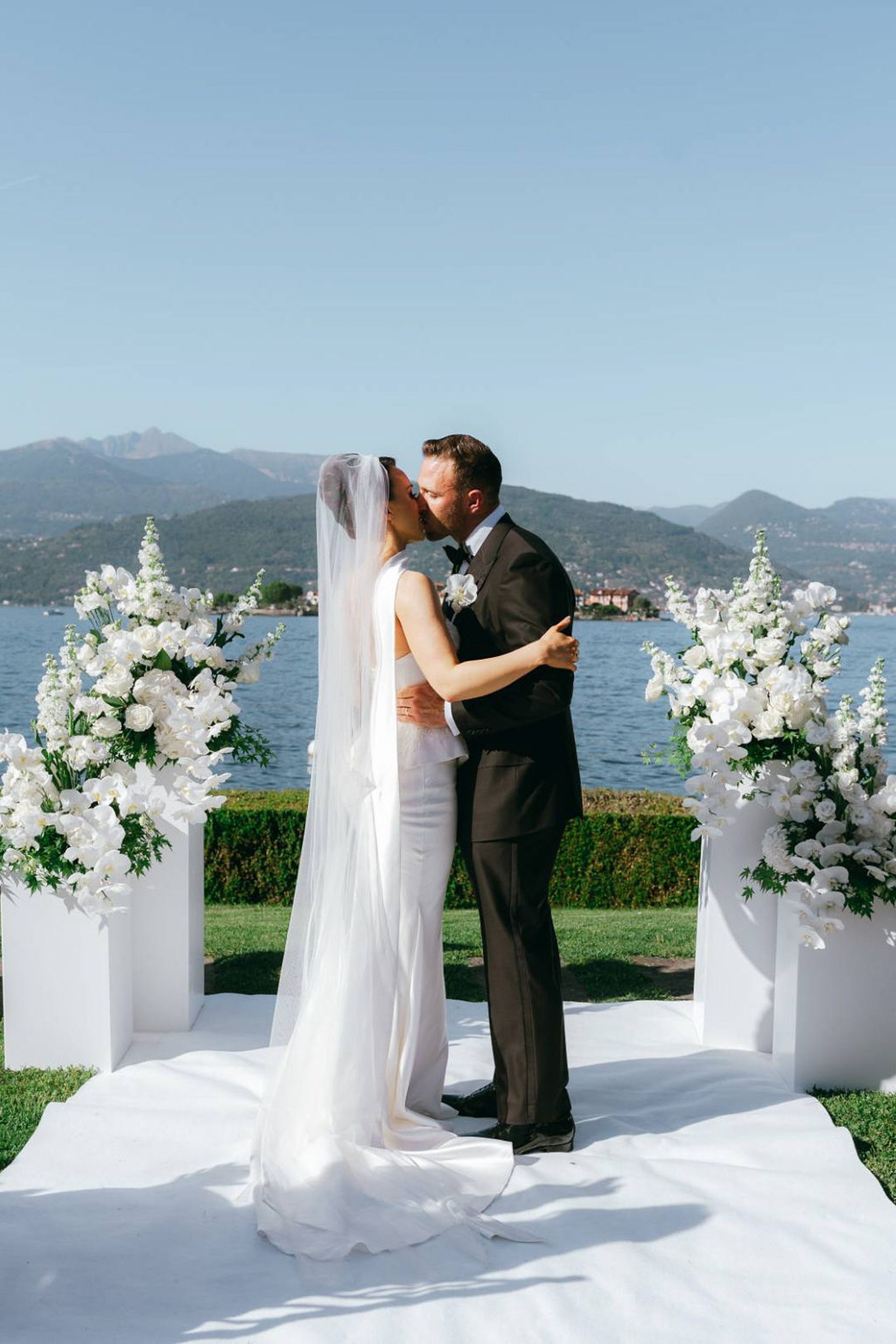 Newlyweds sharing their first kiss at a lakeside small wedding in Italy with mountain scenery