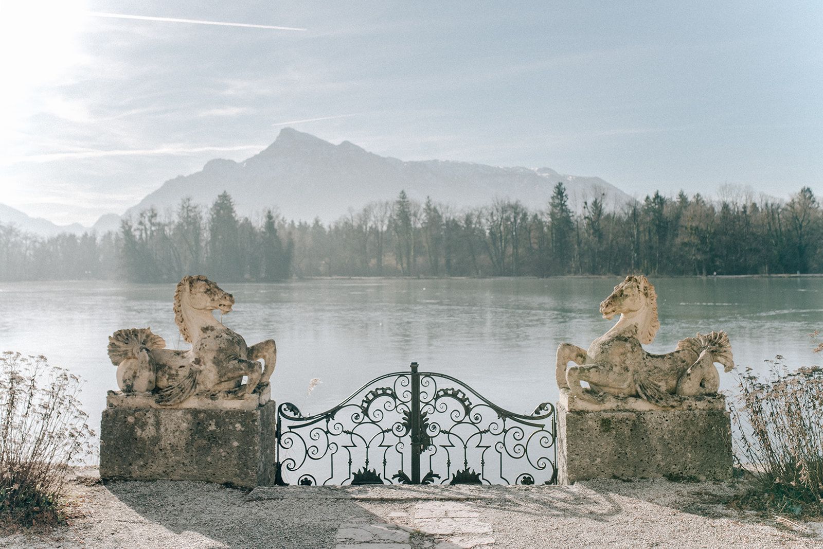 Stone horse statues and wrought-iron gate at a misty lake near Salzburg in winter