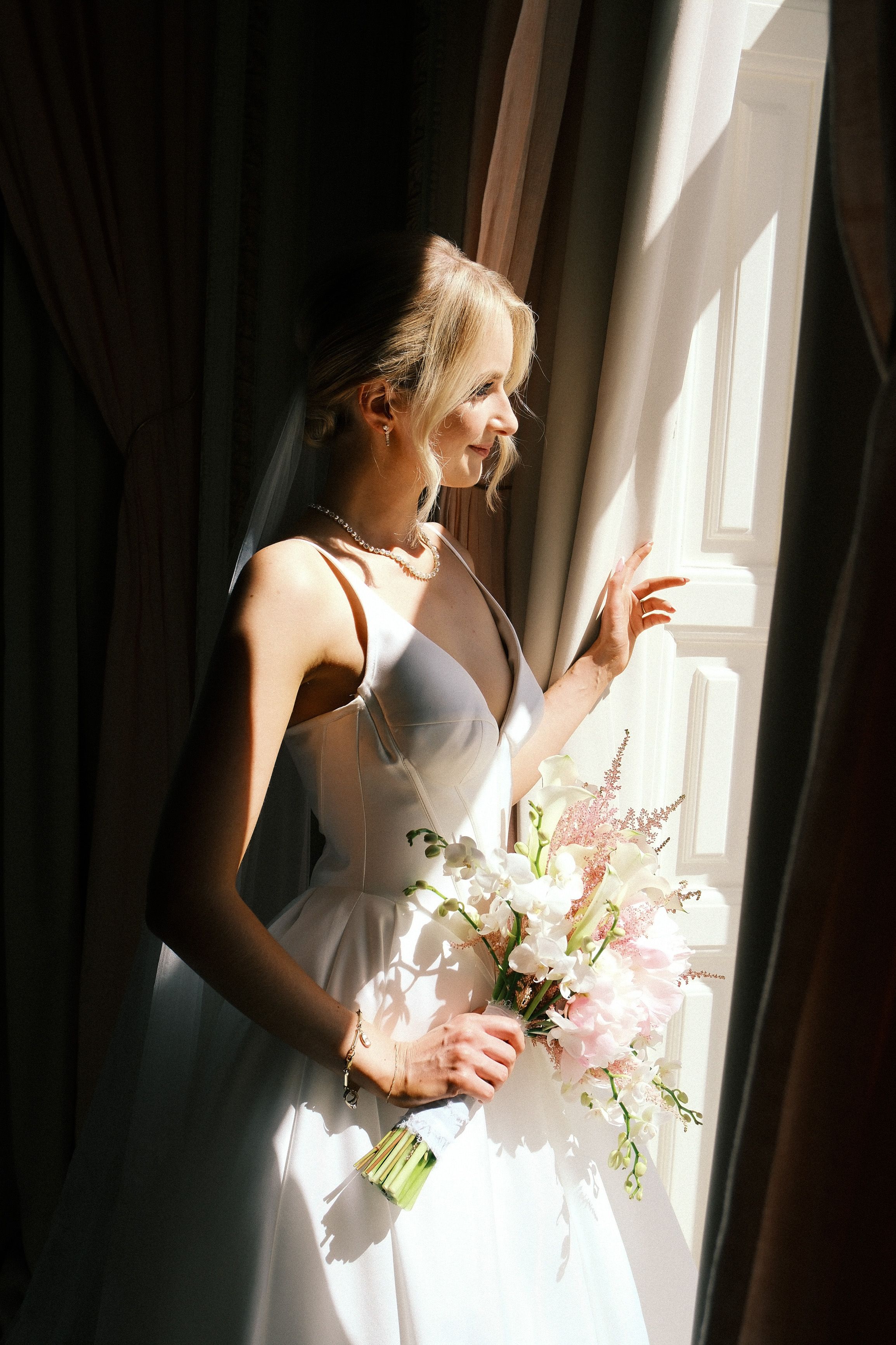 Bride holding a pastel bouquet by a window before her small wedding in Portugal