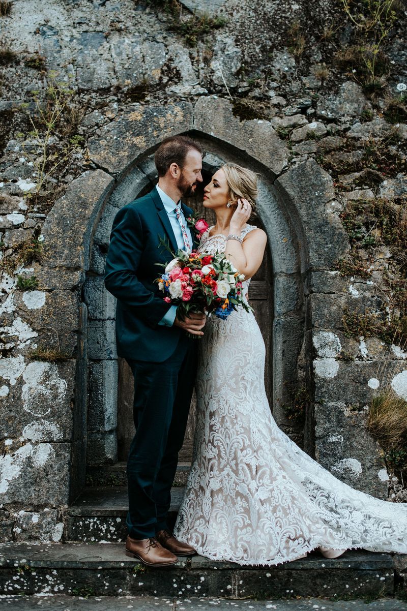 Bride and groom romantically looking at each other with medieval castle walls in the background during their destination elopement in Ireland