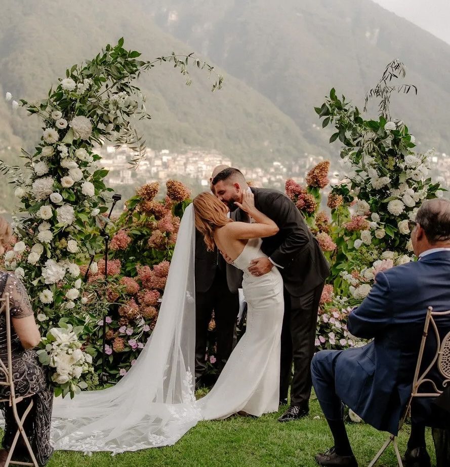 Bride and groom kissing during a wedding ceremony in Italy with Lake Como and rolling hills in the background