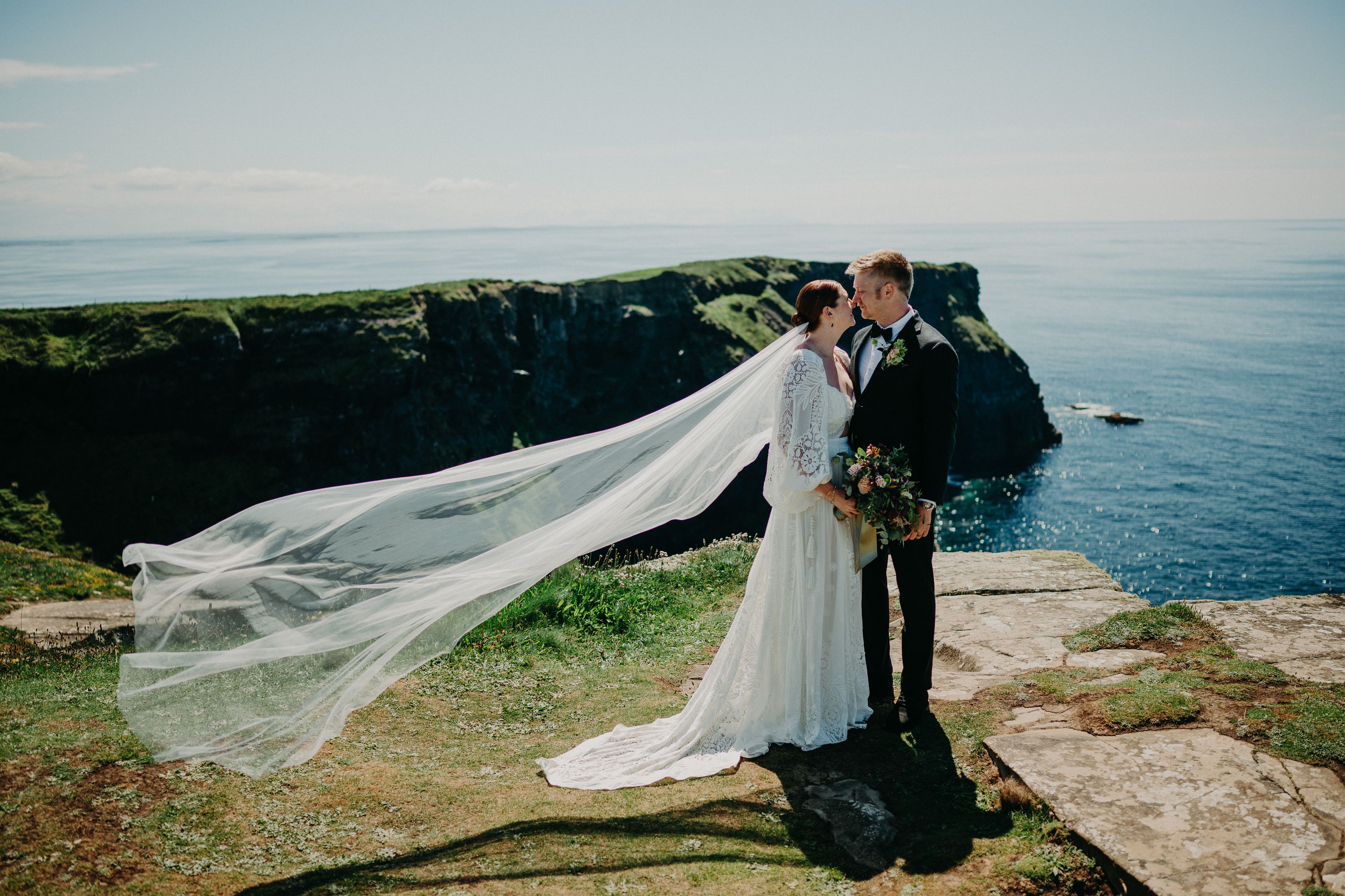 A bride and groom looking at each other during their small wedding in Ireland set in a beautiful cliff with the sea behind them