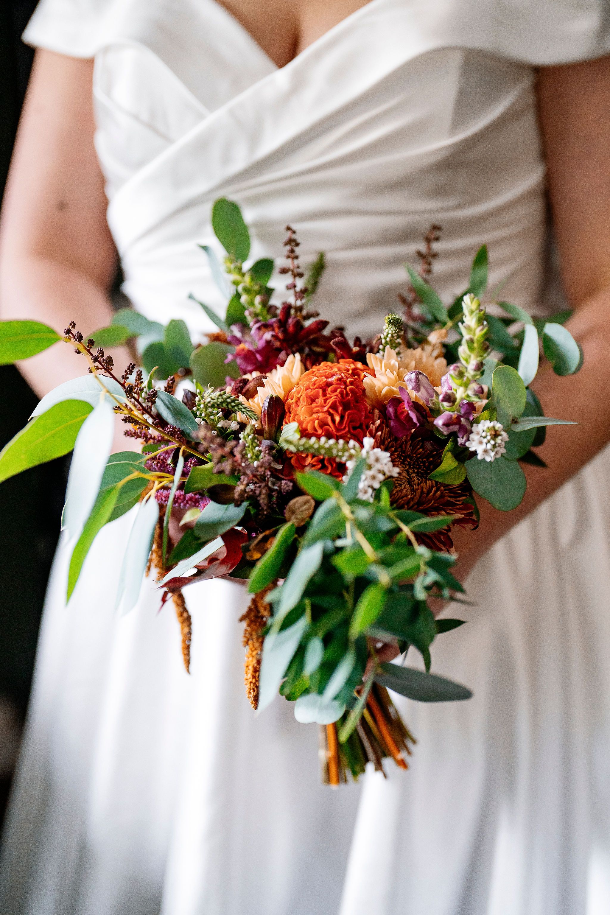 Bride's arms and hands hold a bouquet with autumn colors during her elopement in Ireland