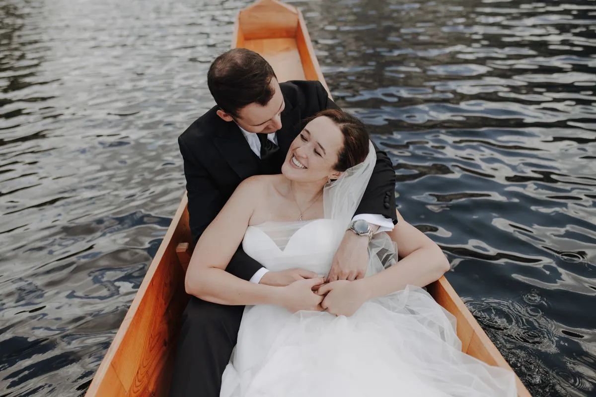 Newlyweds cuddling in a wooden boat on an Alpine lake after their symbolic ceremony