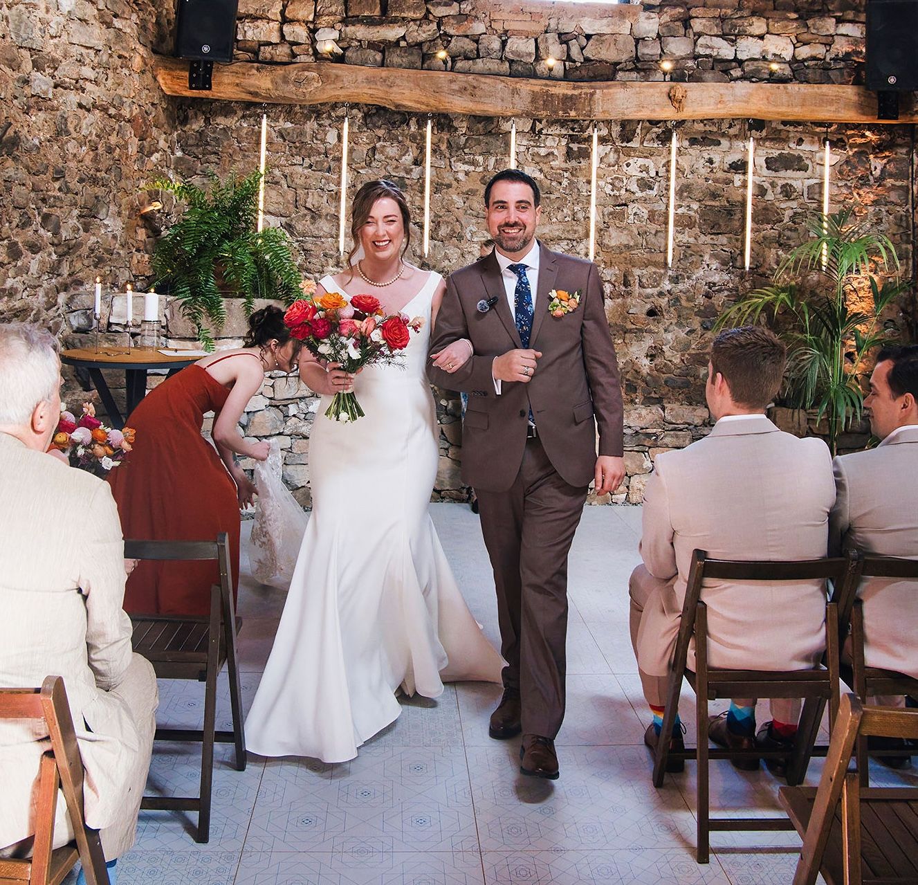 Bride and groom walking down the asile during their indoor wedding ceremony in Spain with a brick wall in the background