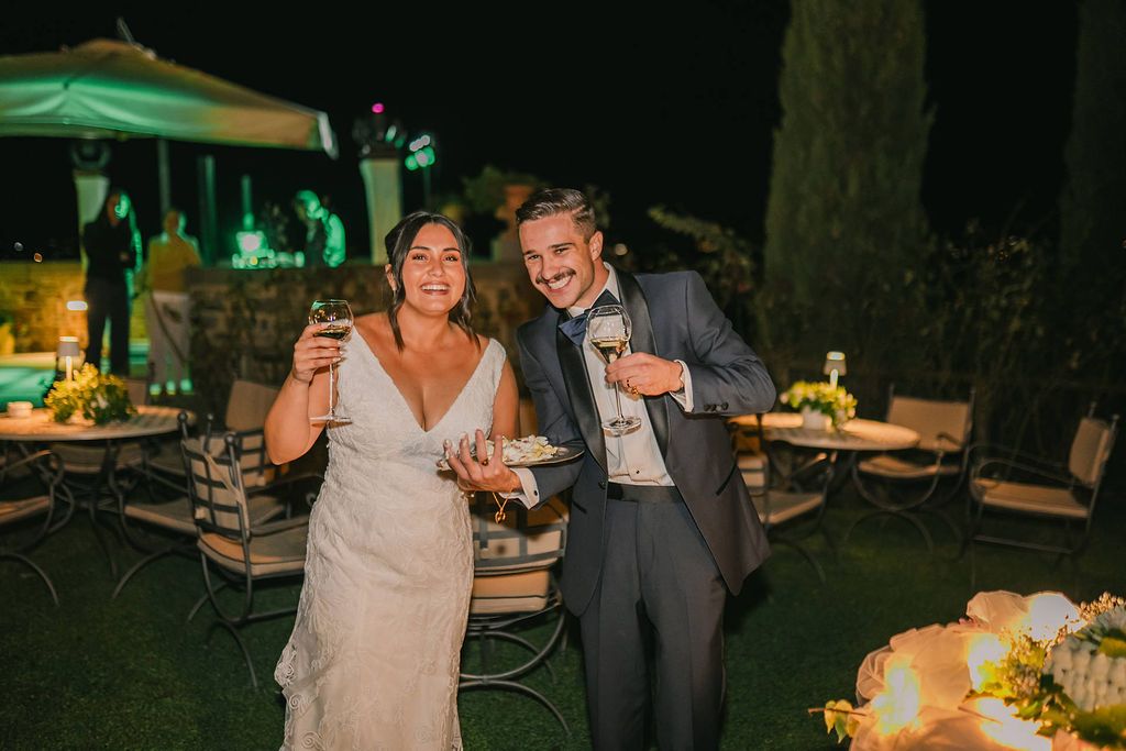 Newlyweds smiling and holding wine in an evening celebration of their destination wedding in Italy