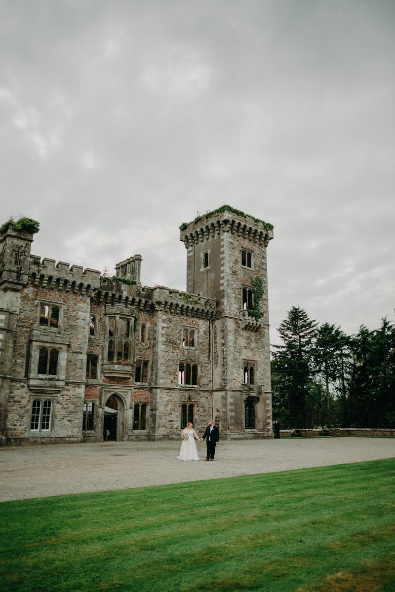 Bride and groom walking in a large estate with a castle ruin in the background during their elopement in Ireland