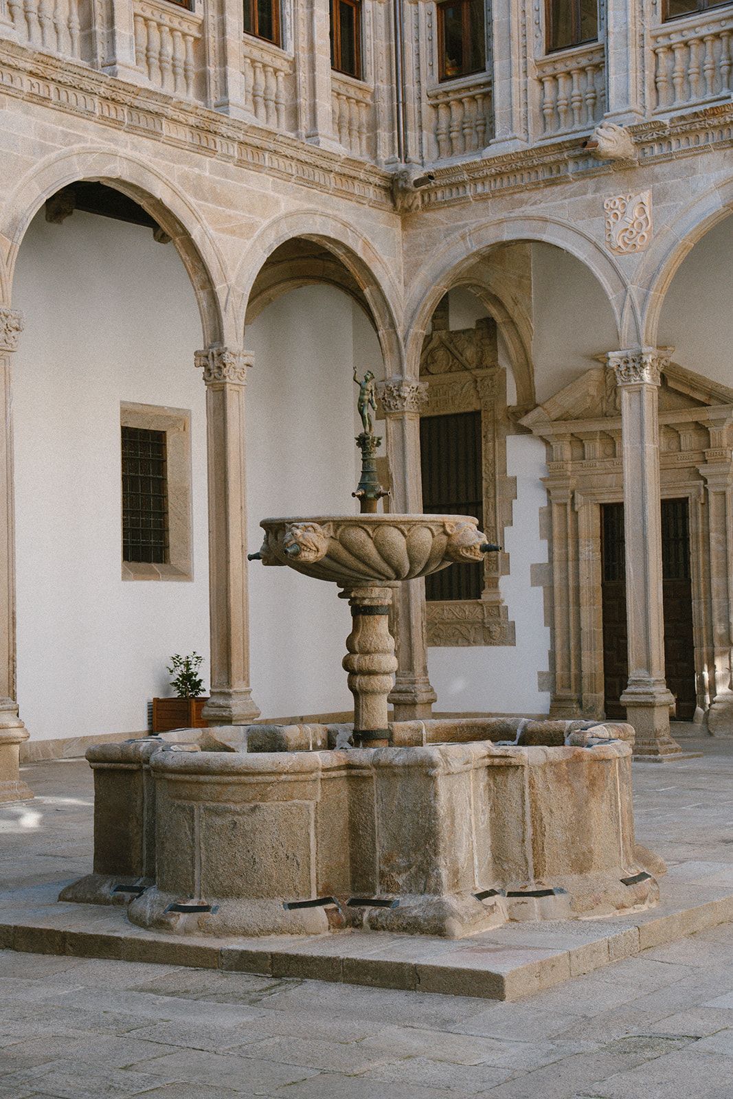 Renaissance cloister fountain with lion-head spouts and carved arcades at the Parador de Santiago de Compostela.