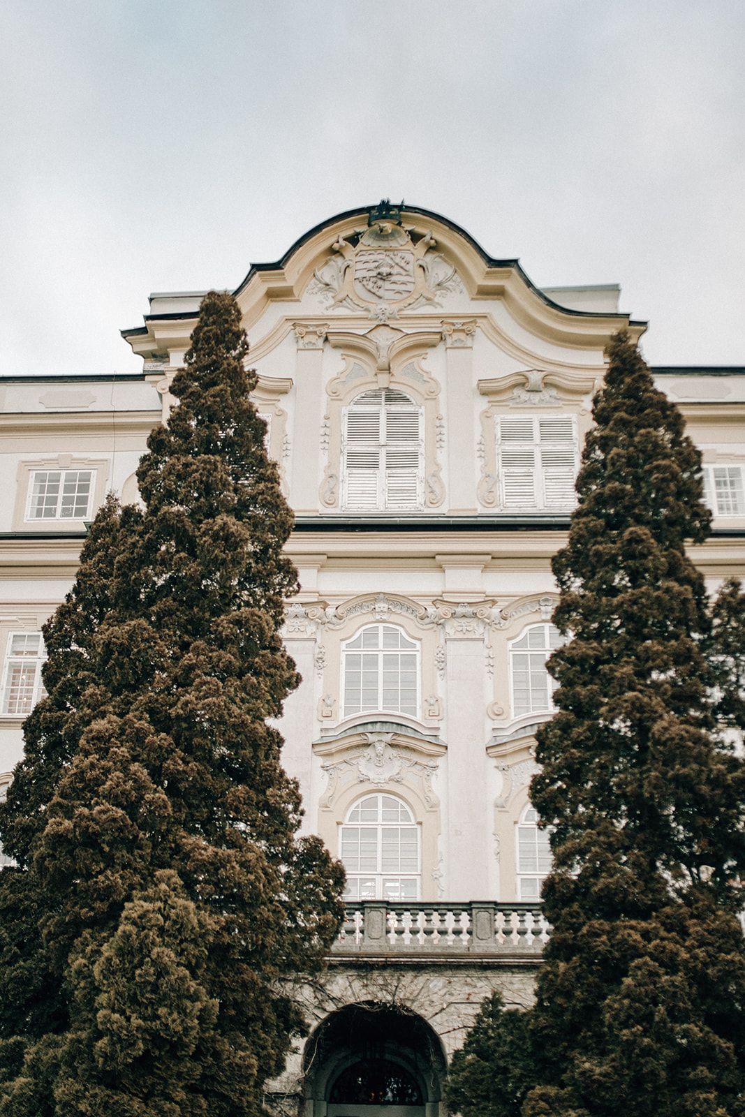 Baroque palace facade rising between two old conifers in Salzburg