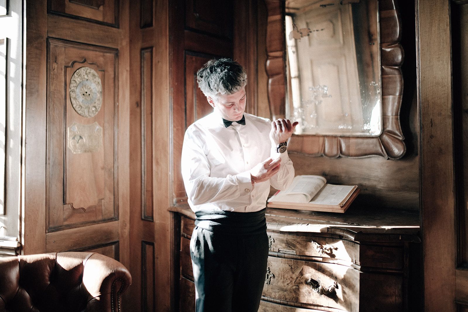 Groom fixing his cuffs in a wood-panelled castle dressing room