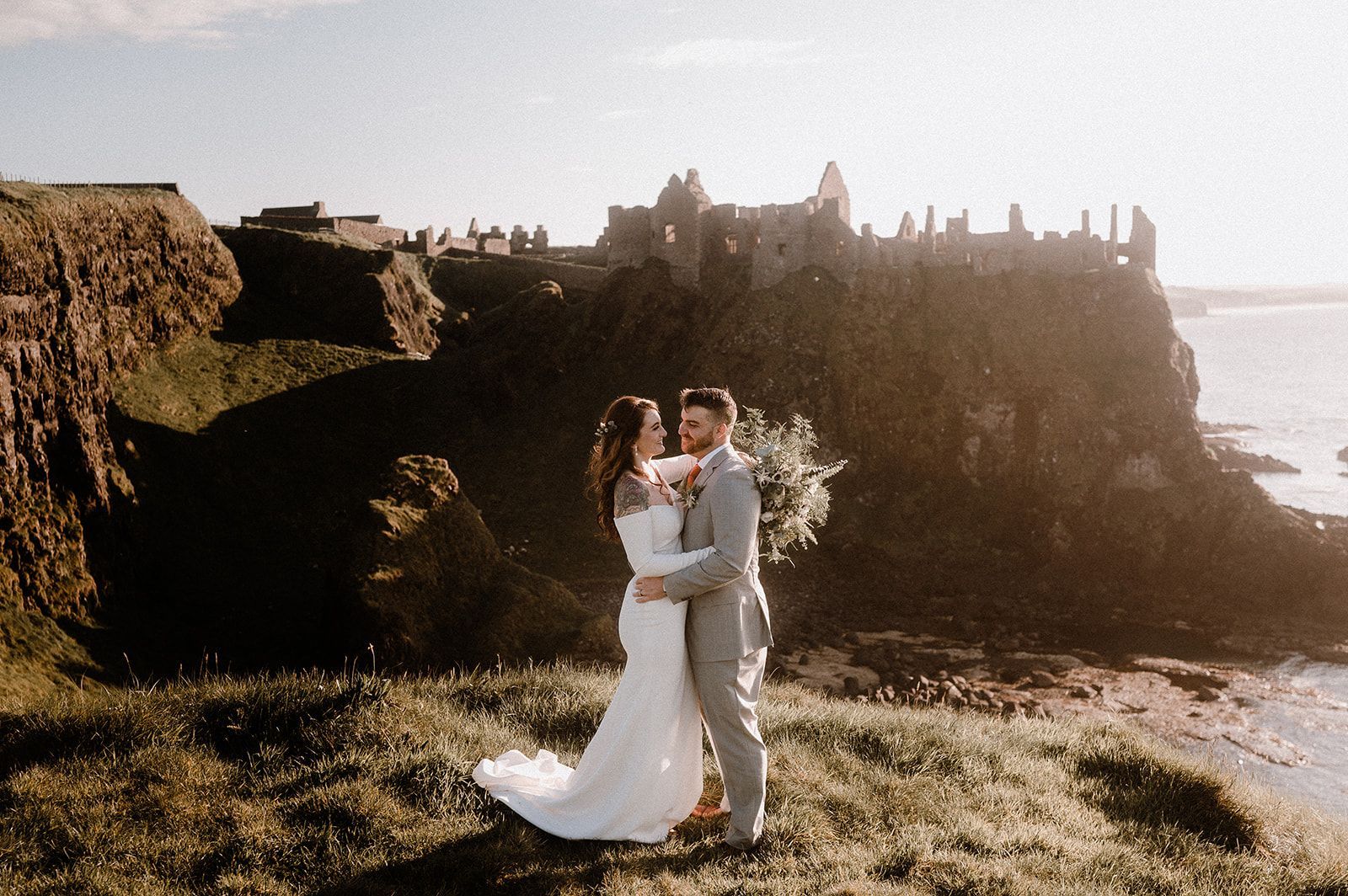 Bride and groom holding eachother at their wedding ceemony in front of Dunluce Castle in Northern Ireland