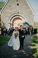 Newlyweds with the chapel and their guests in the background during the photoshoot of their intimate wedding in Ireland