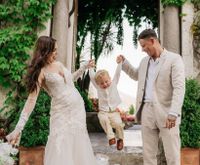 Bride and groom side by side helping each other lift their son who's in the middle, enjoying the activity
