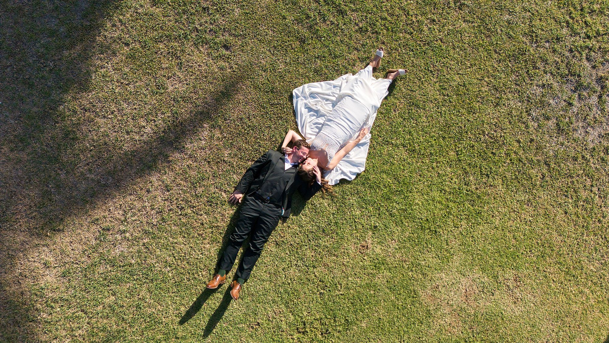 A drone shot of the bride and groom who are lying on the grassy estate of the farmhouse where they got married in Spain