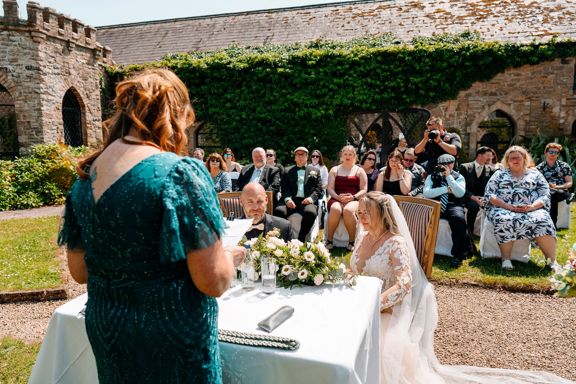 Bride and groom, with their guests and celebrant seated in a castle garden for the ceremony of their small wedding in Ireland