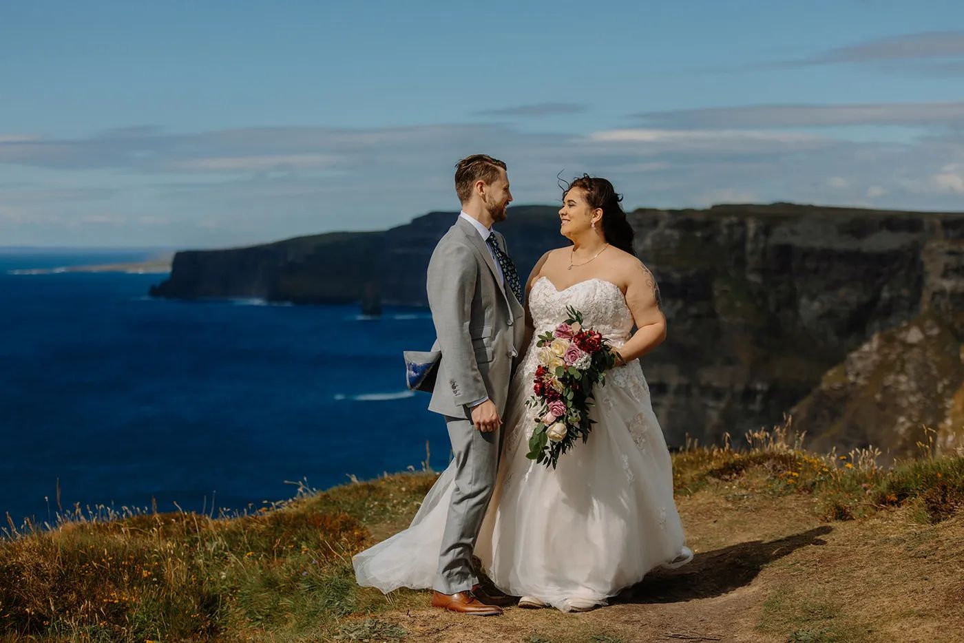 Bride holding a bouquet with her groom on a bright day atop the Cliffs of Moher