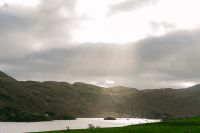 Sun shining through the gloomy autumn clouds of Ireland down to a lake surrounded by hills