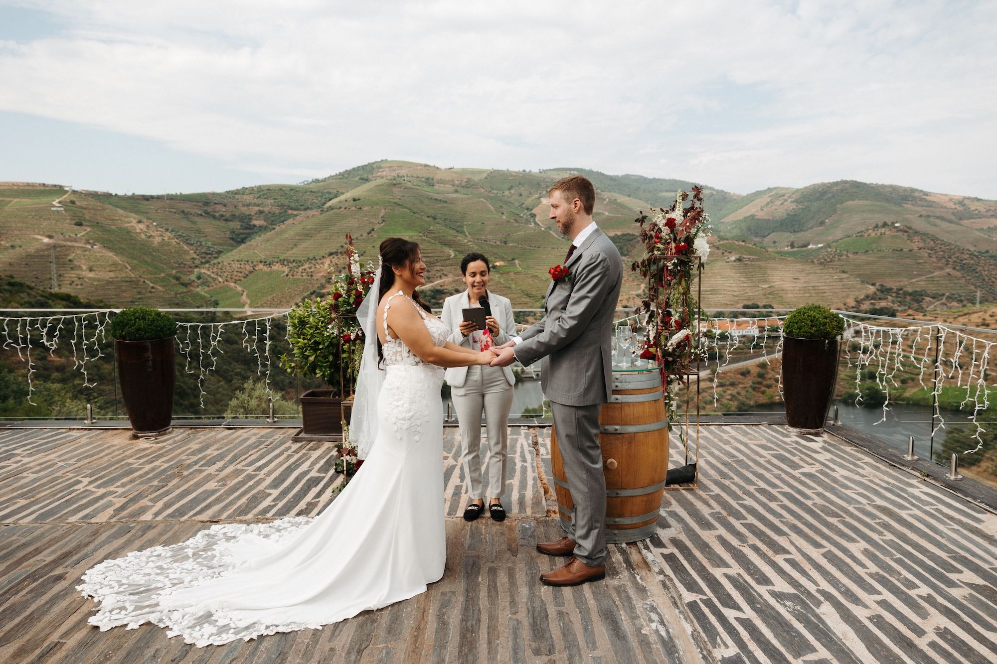 Bride and groom hold hands in front of their celebrant during their small wedding in Portugal with mountains as the backdrop