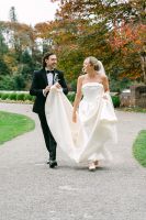 Newlyweds laughing while walking as the groom holds his bride's dress trail during their Irish wedding photoshoot