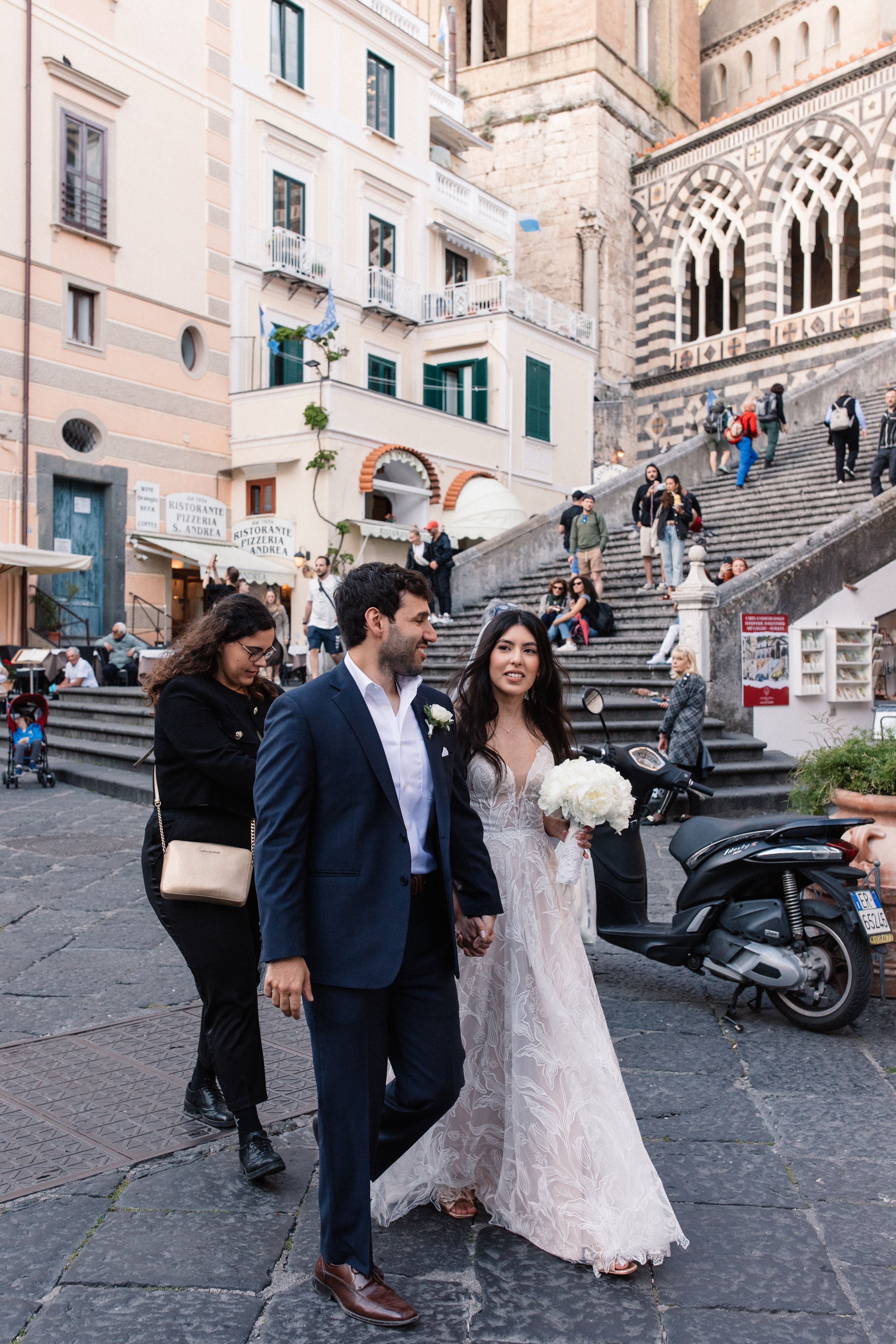 Bride and groom walking along a street in Amalfi for their elopement in Italy with a church in the background
