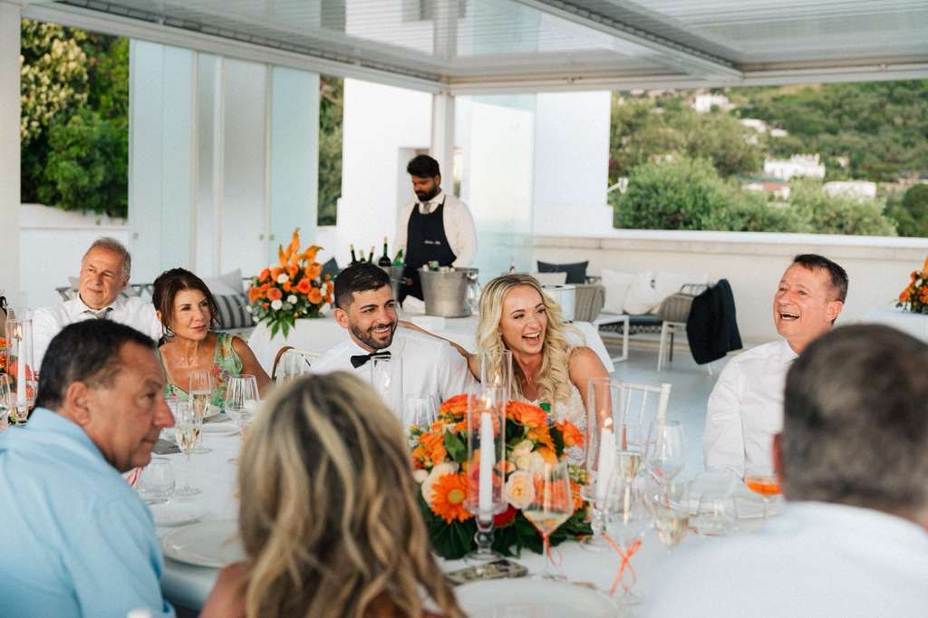 Bride laughs beside her groom while seated and chatting with guests during the reception of their small wedding in Italy