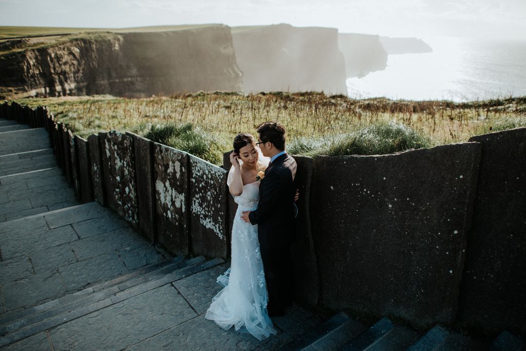 Bride and groom at a retaining wall with Cliffs of Moher and the Atlantic in the background during their elopement in Ireland