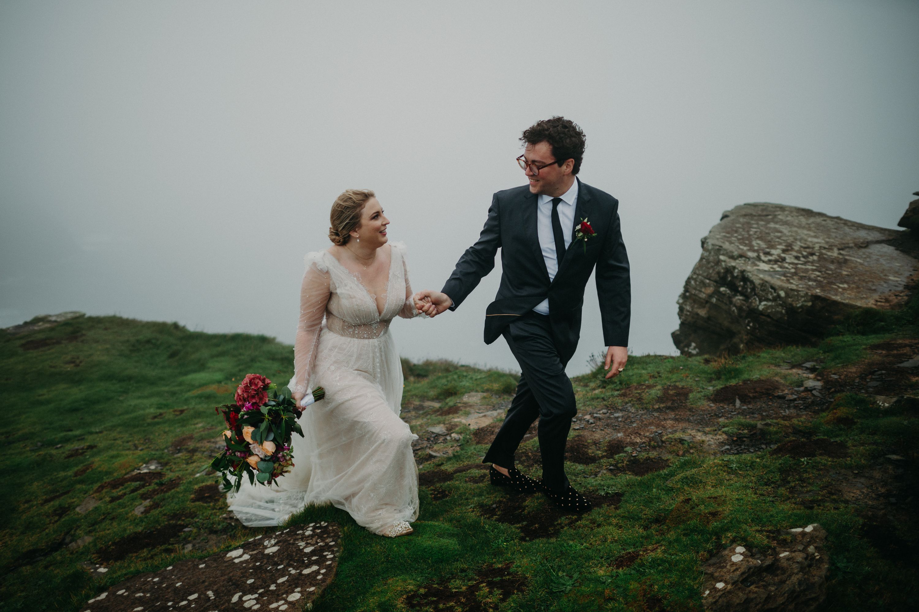 Newlyweds holding hands on a foggy cliffside path after a small wedding in Ireland