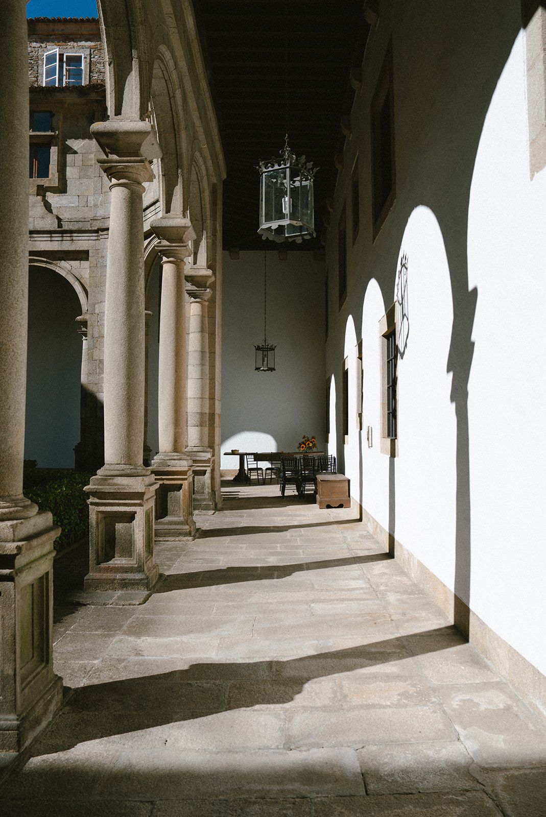 Sunlit cloister gallery with granite columns, iron lanterns and a sunflower-dressed table ready for a wedding ceremony.